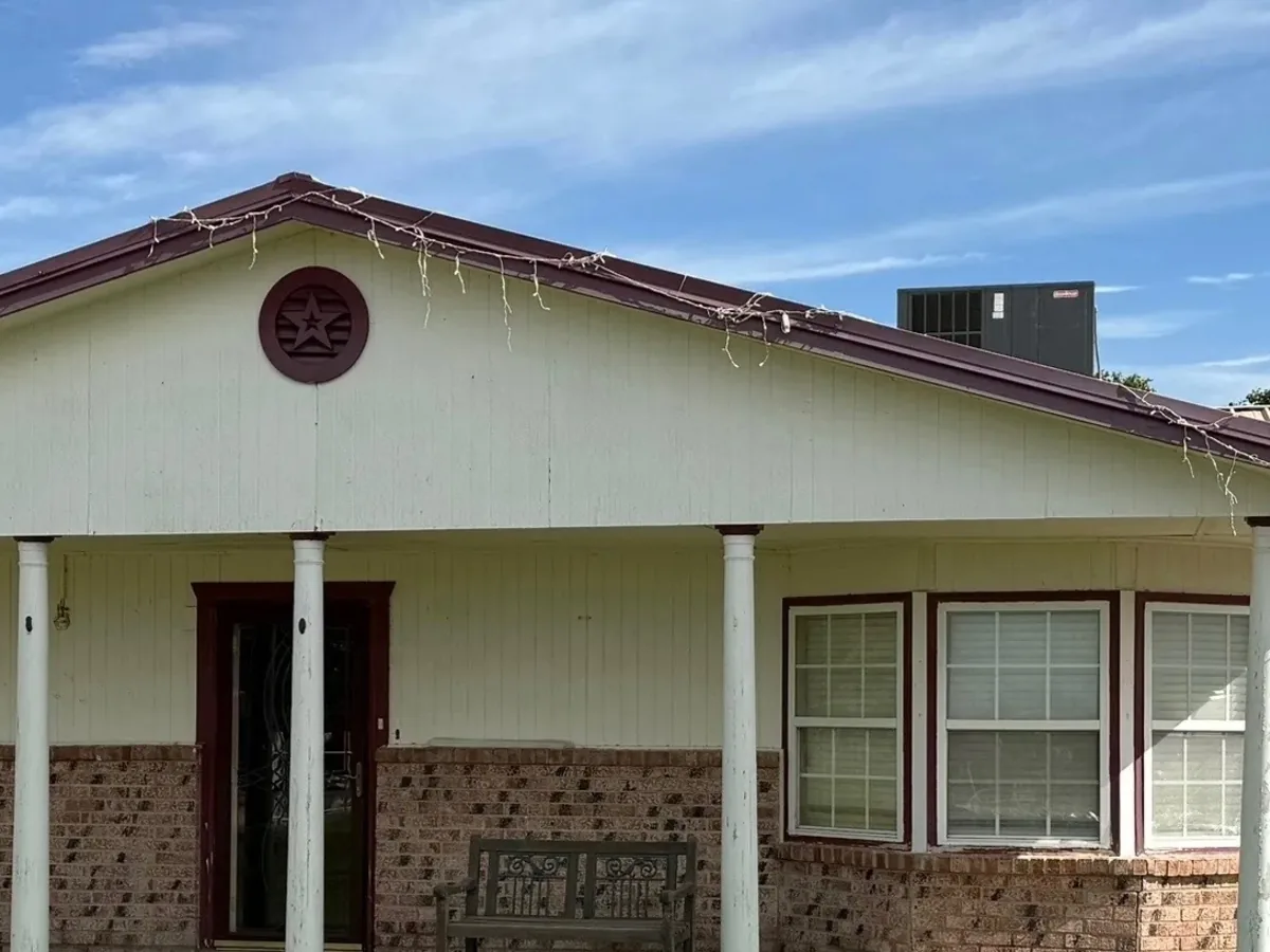 Front of a brick home with beige siding and white columns before repainting
